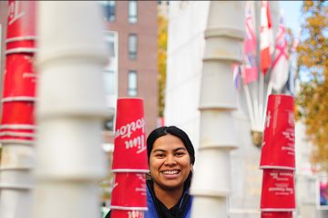 UBC student smiles at camera from behind structure made from used coffee cups.